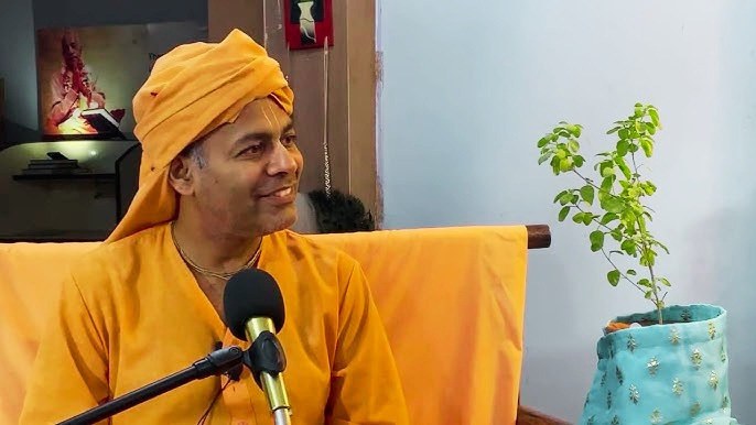 His Grace Keshavananda Das speaking with a microphone beside a Tulsi plant